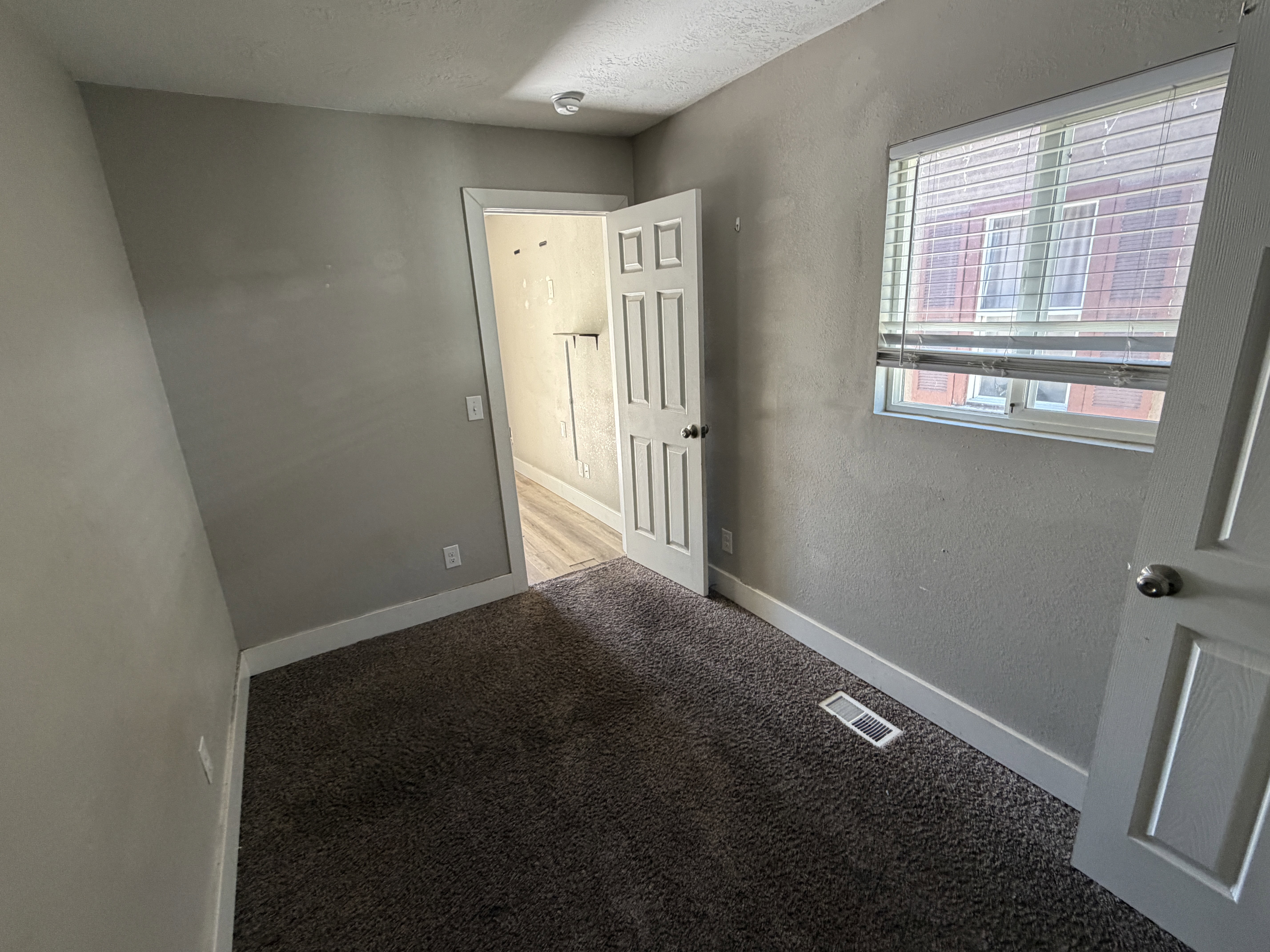 Carpeted room with a window featuring horizontal blinds