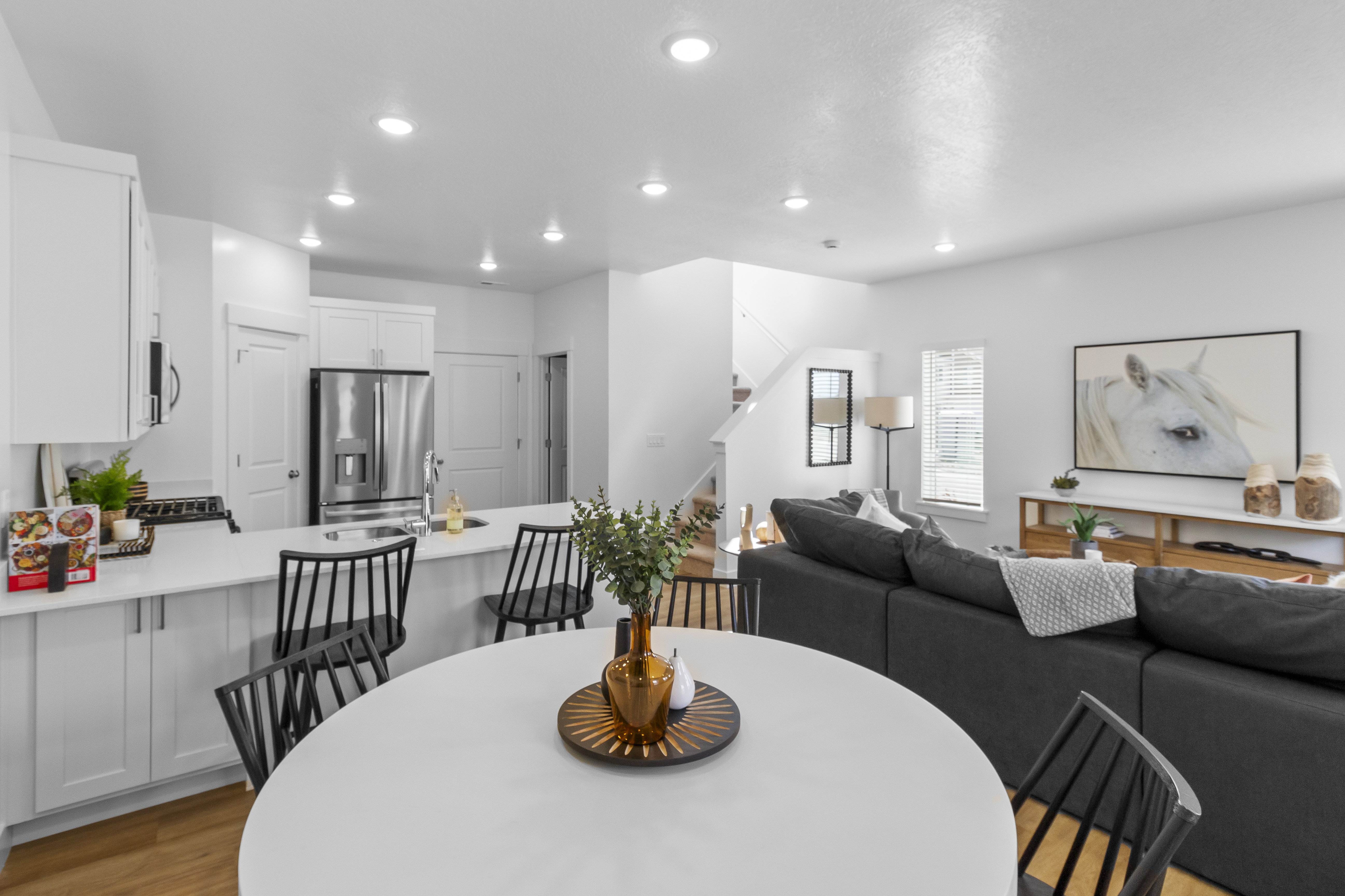 Open-concept living space featuring a kitchen island with seating, stainless steel refrigerator, white cabinetry, recessed lighting, and wood-finish flooring