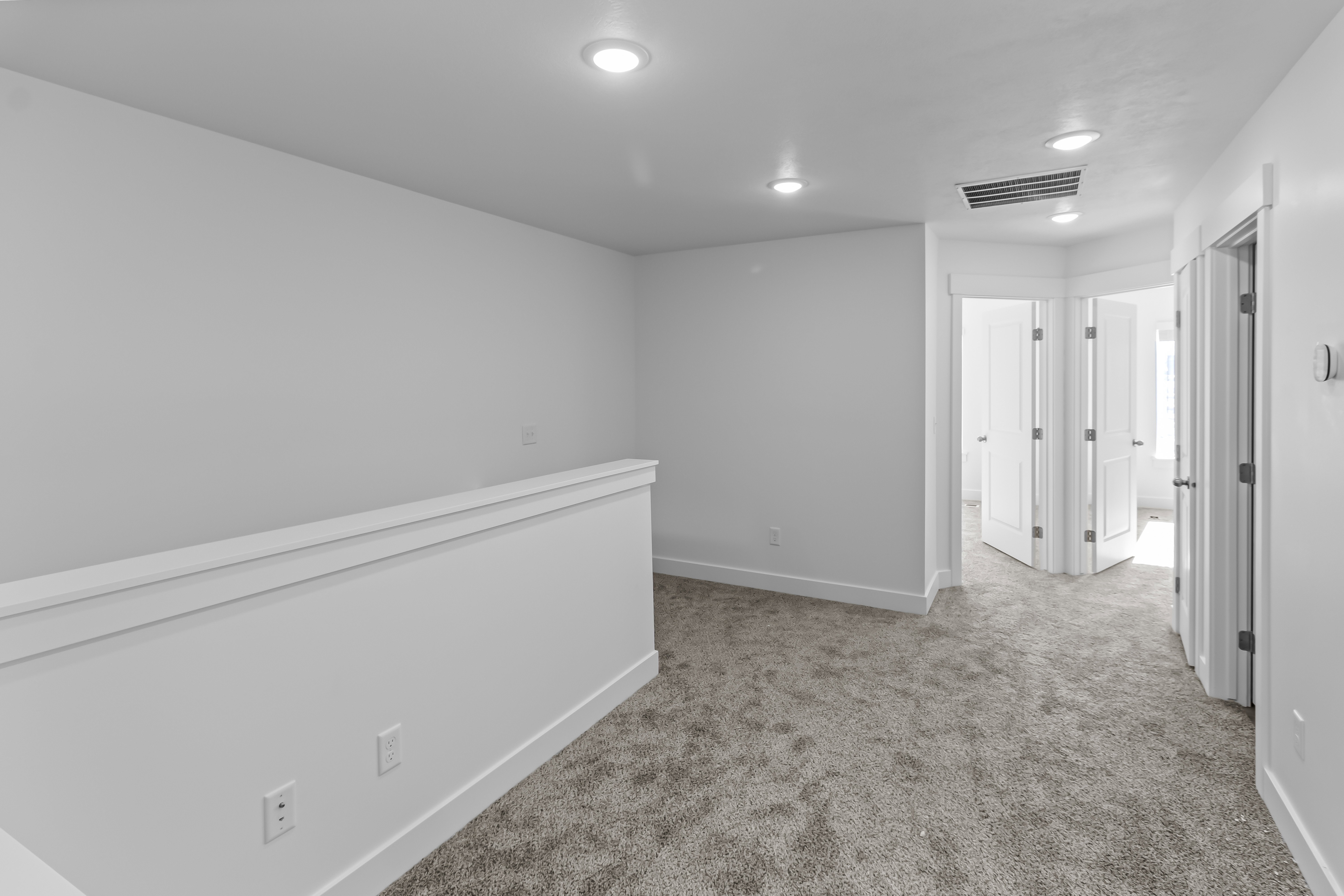 Carpeted hallway featuring a white half-wall railing, recessed lighting, and multiple white panel doors