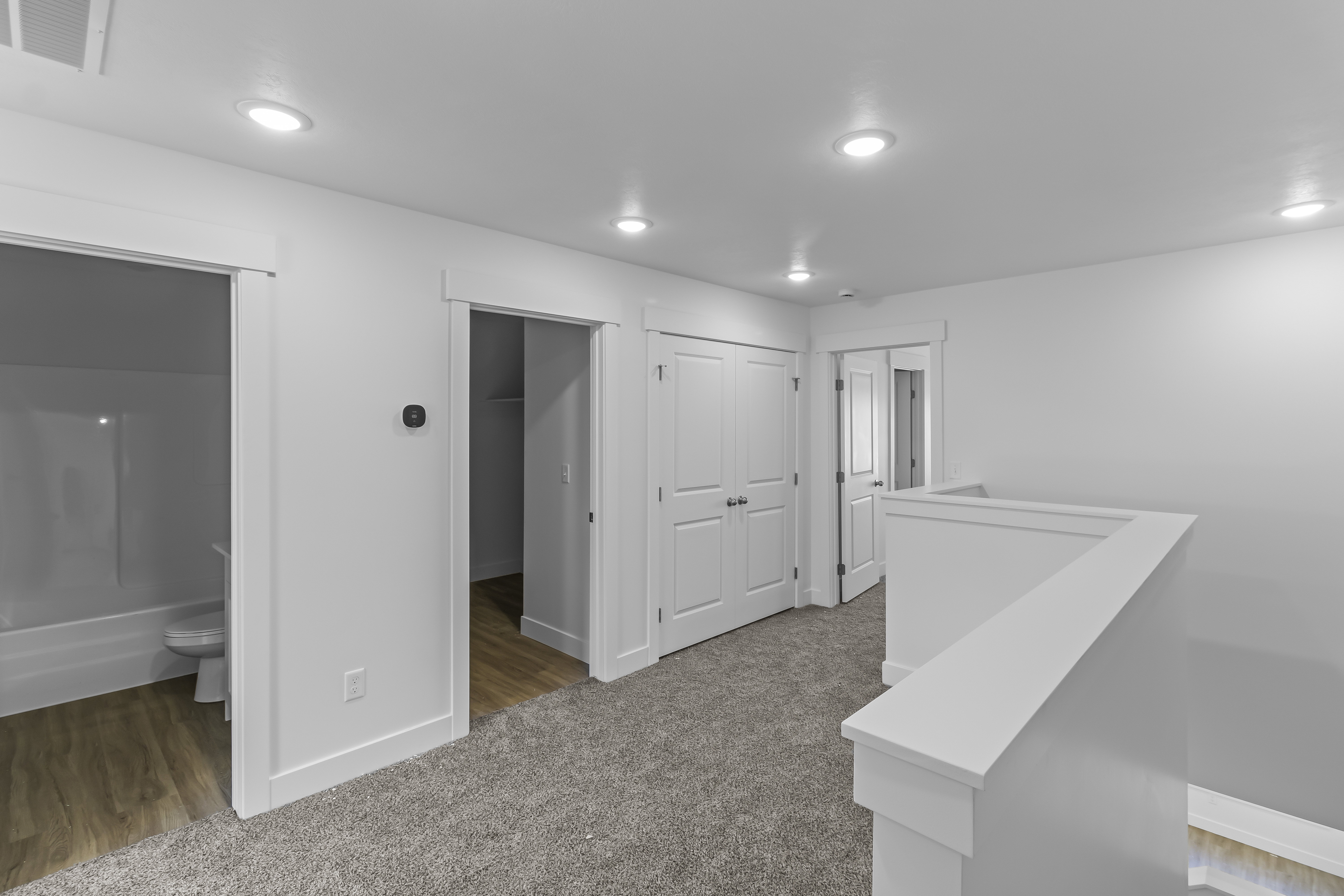 Carpeted hallway featuring bright recessed lighting, white walls, multiple doorways, and a white balustrade