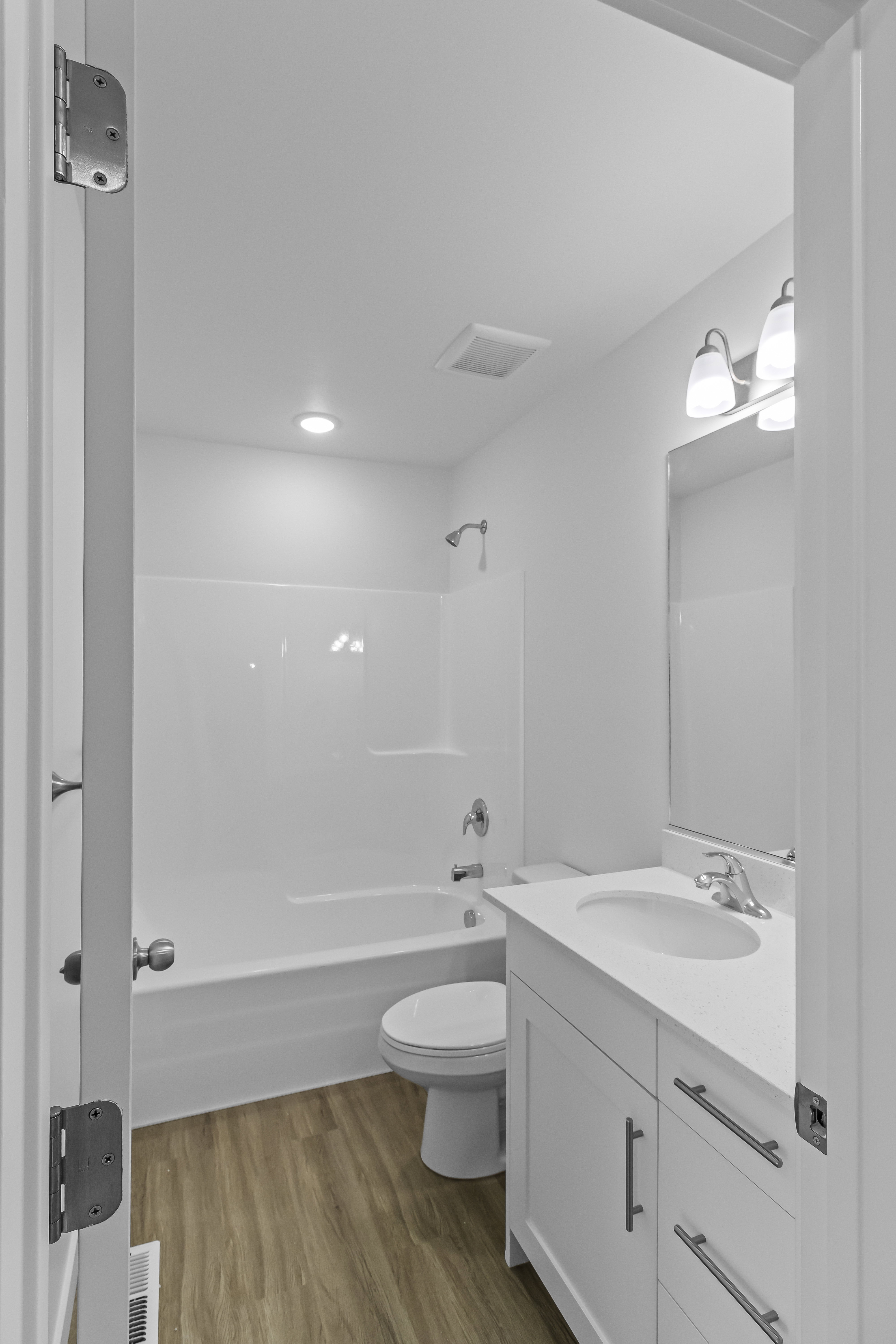 Full bathroom featuring a white vanity with a single basin sink, white bathtub with shower, and wood-finish flooring