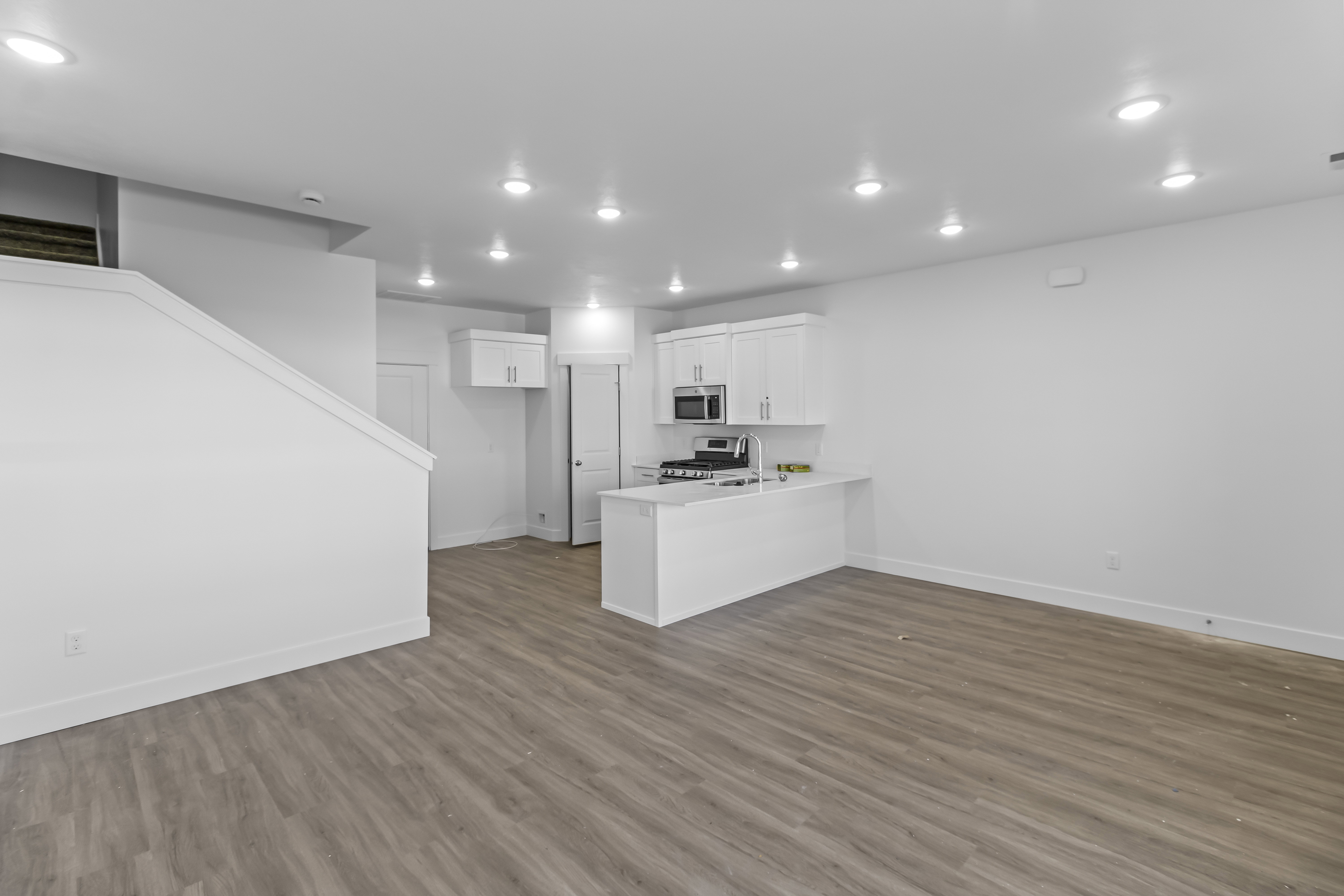 Expansive open-concept living area featuring wood-finish flooring, recessed lighting, and a white kitchen with stainless steel appliances