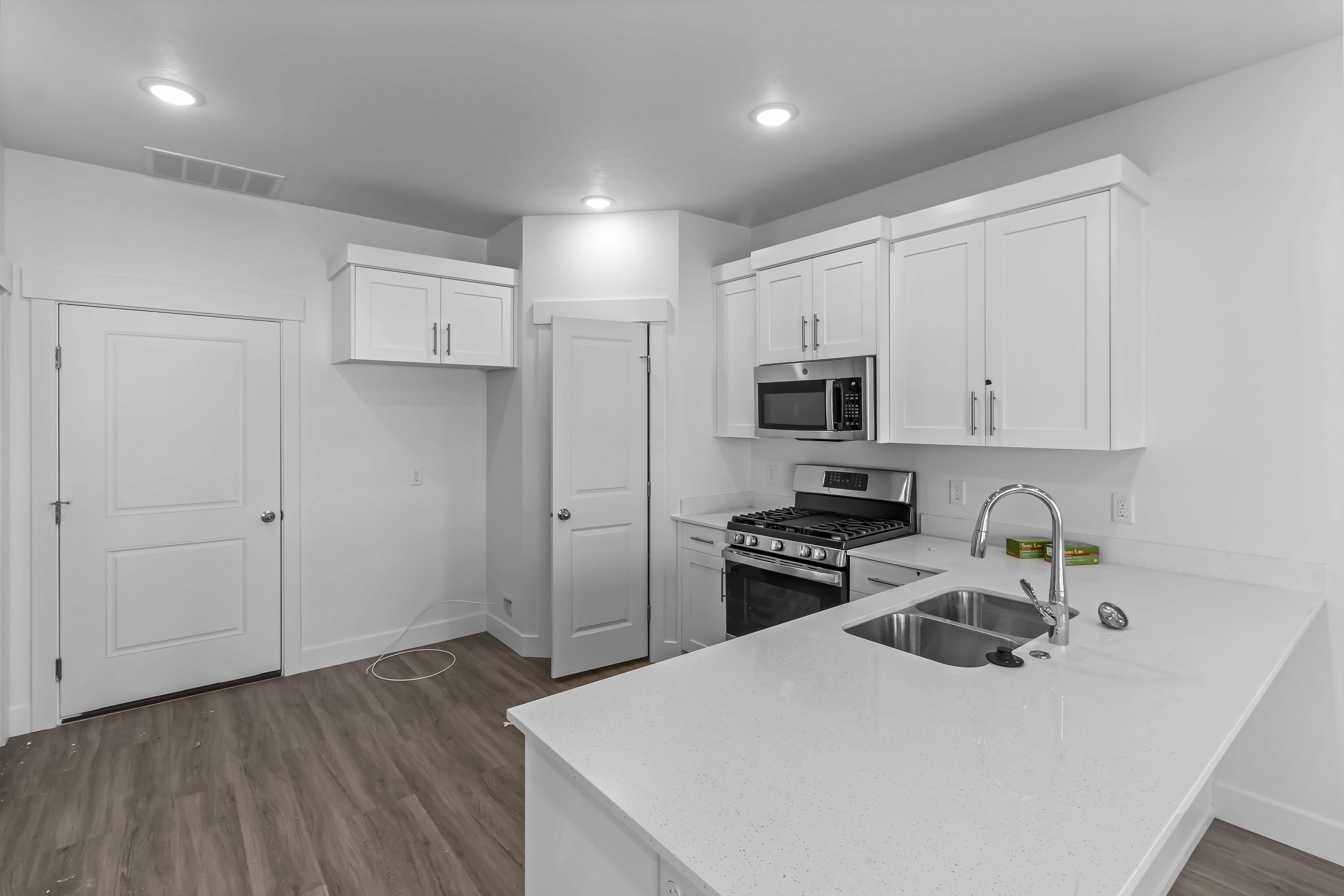 Contemporary kitchen featuring white shaker cabinetry, stainless steel appliances, a double basin sink, light-toned countertops, and wood-finish flooring