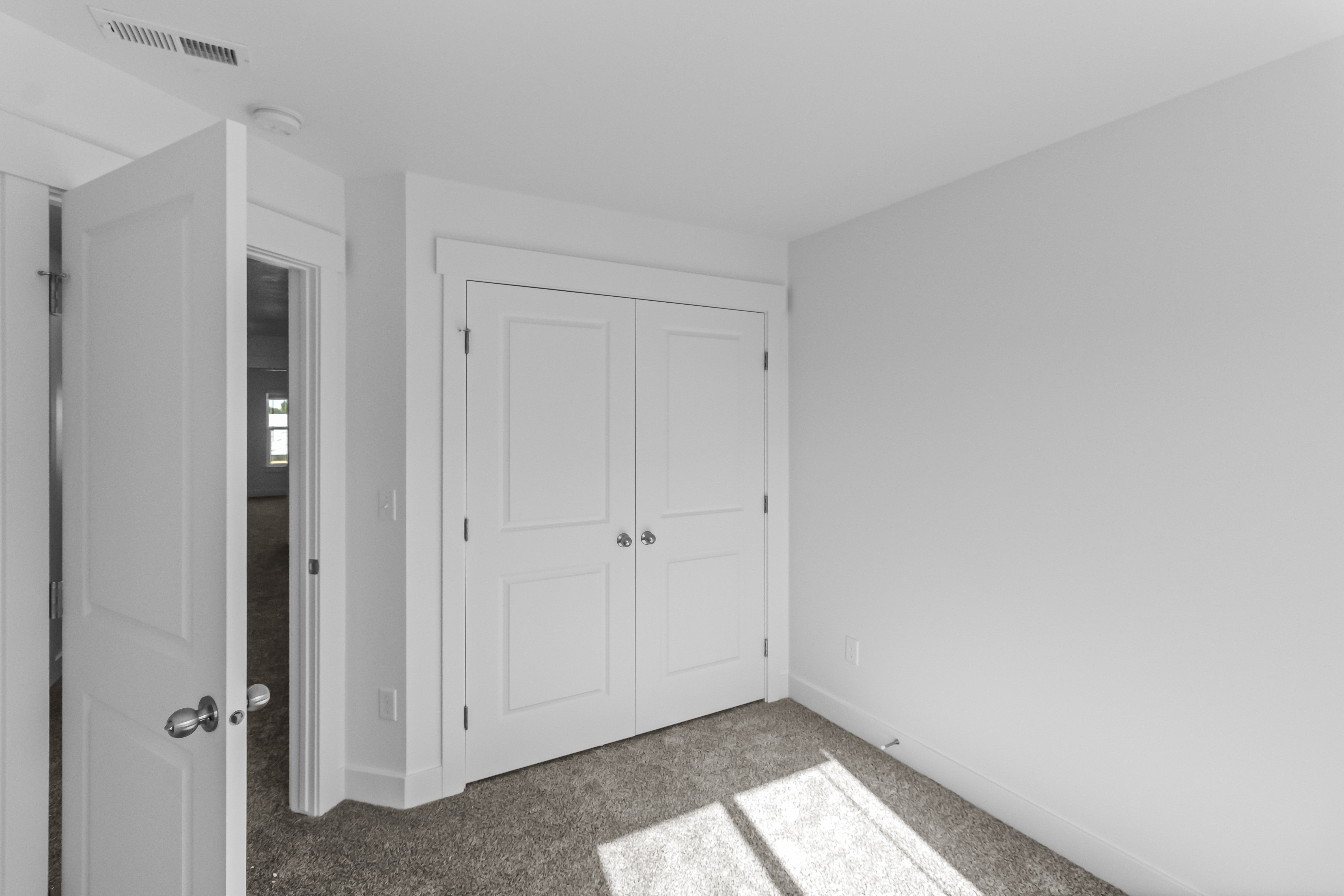 Bedroom featuring light gray carpeting, crisp white walls, and a recessed panel bi-fold closet door with chrome hardware