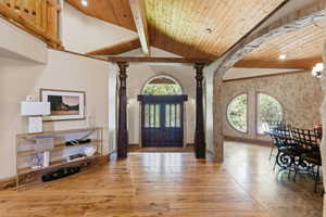 Entryway featuring wood-finish flooring, exposed wood beams, a prominent dark wood double door, and stone archways