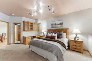 Carpeted bedroom with a built-in wooden desk, integrated cabinetry featuring glass-front doors, and track lighting