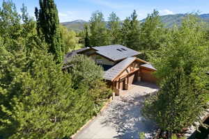 Contemporary architecture featuring a dark metal roof, natural wood accents, a paved driveway, and surrounding mature trees