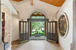 Grand entryway featuring arched double doors with glass panels, wood-finish ceiling, exposed wood beams, and a stone accent wall