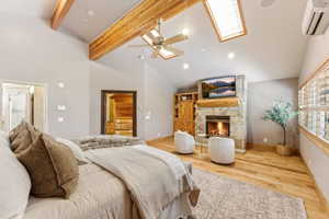 Vaulted ceilings with exposed wood beams define this space, featuring a stone-faced fireplace with a natural wood mantle, skylights, wood-finish flooring, and a ceiling fan