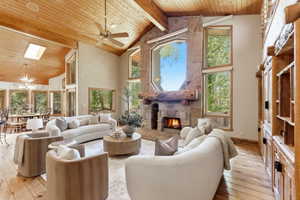 Spacious living area featuring a stone fireplace with a log mantle, vaulted wood-plank ceiling, and wood-finish flooring