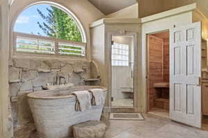 Stone soaking tub with wall-mounted faucet, complemented by a natural stone accent wall and an arched window