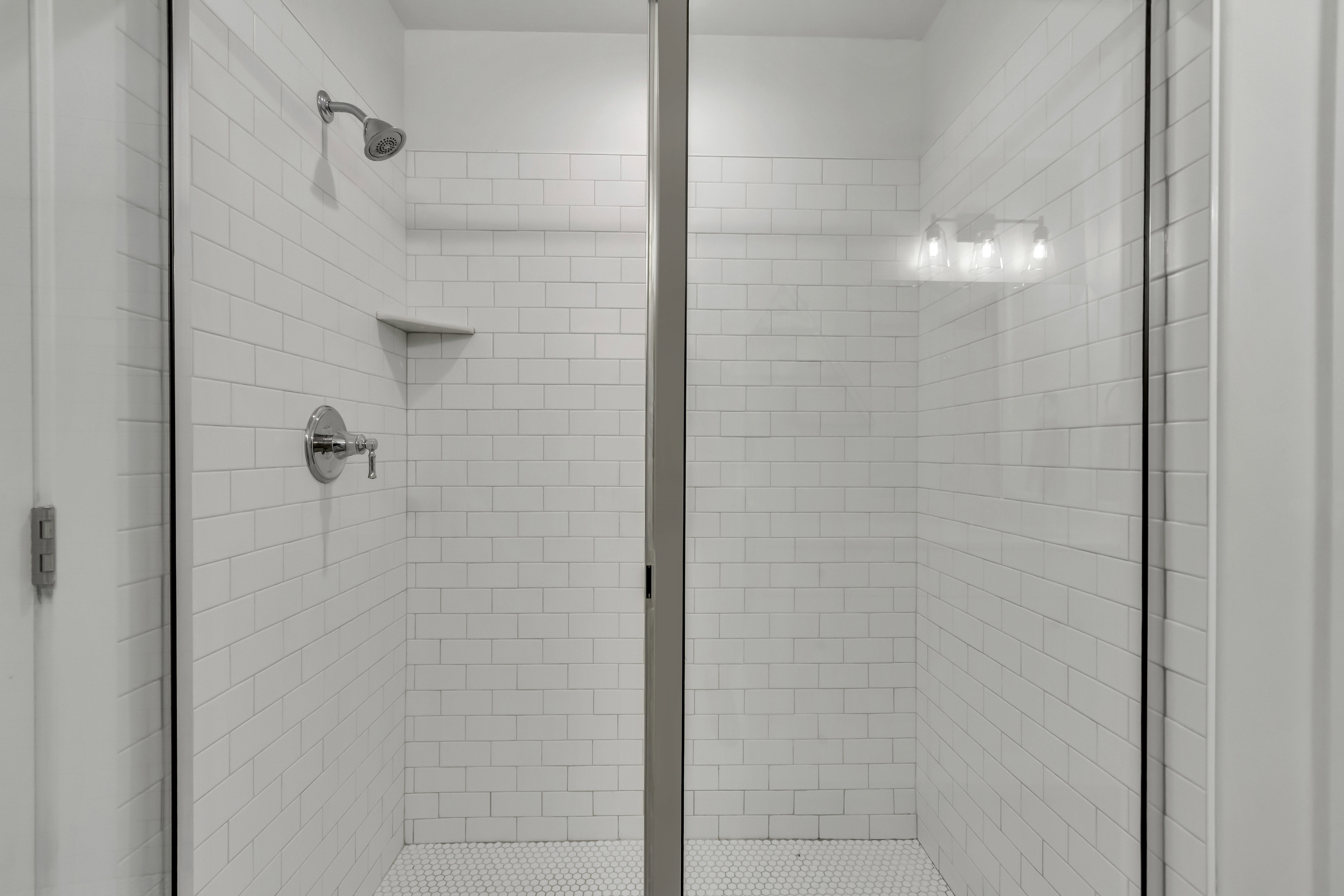 Walk-in shower featuring subway tile walls, a built-in corner shelf, and a hexagonal tile floor