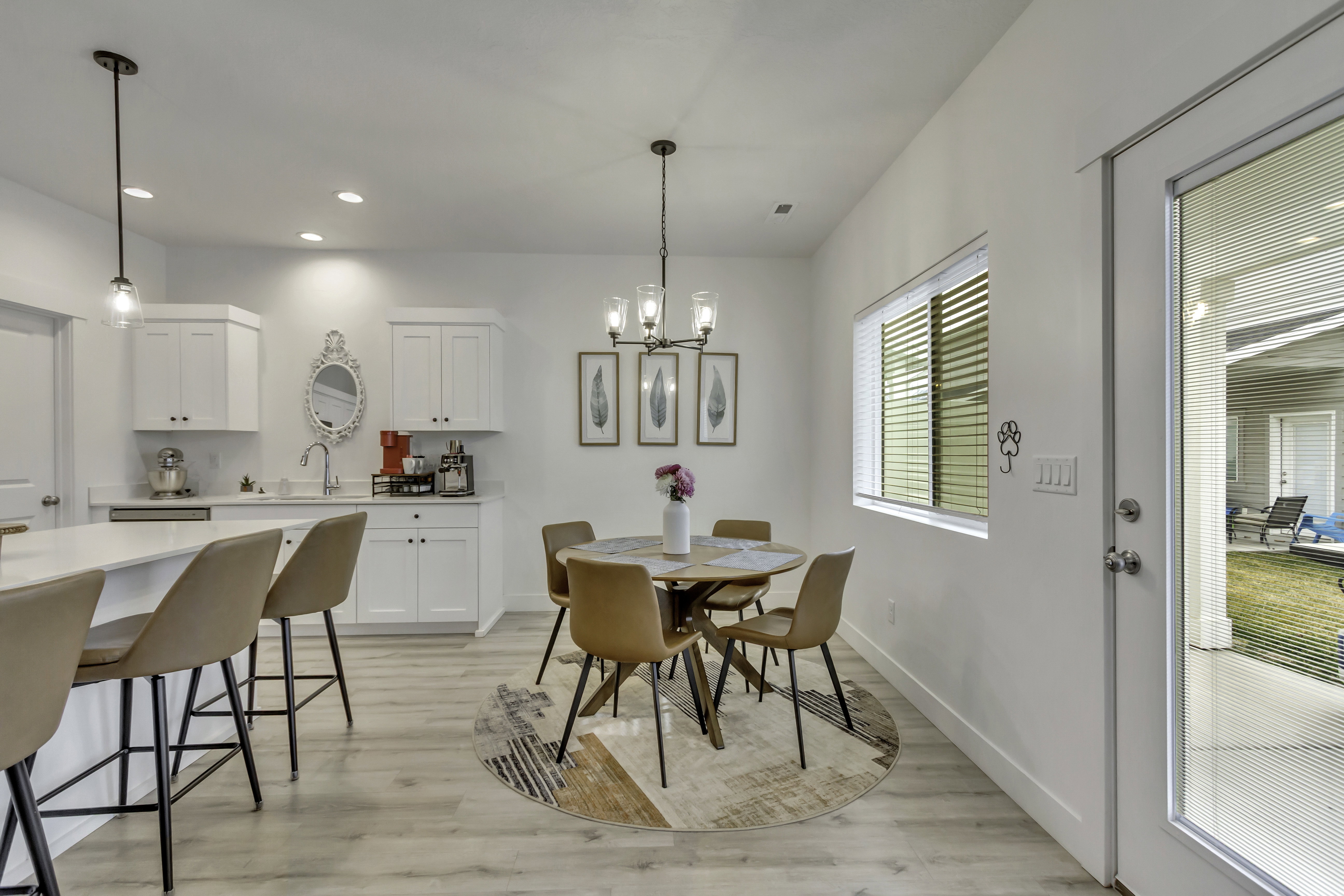 Open-concept living space featuring wood-finish flooring, white cabinetry, a kitchen island with seating, a dining area, and a glass-paneled door leading to an outdoor patio