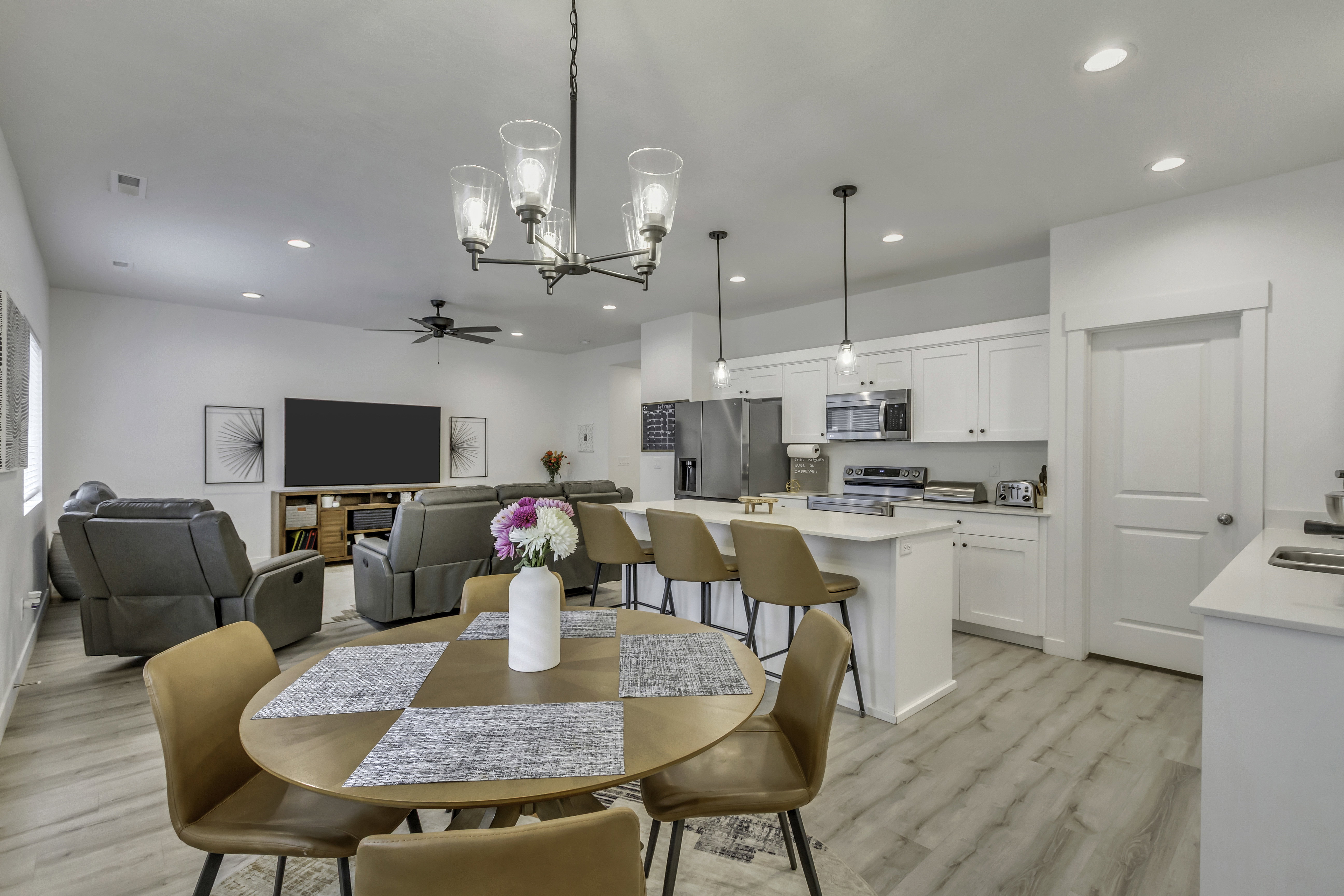 Open-concept living space featuring a dining area with a contemporary chandelier, a kitchen with white cabinetry and a central island, and a living room with recessed lighting and a ceiling fan