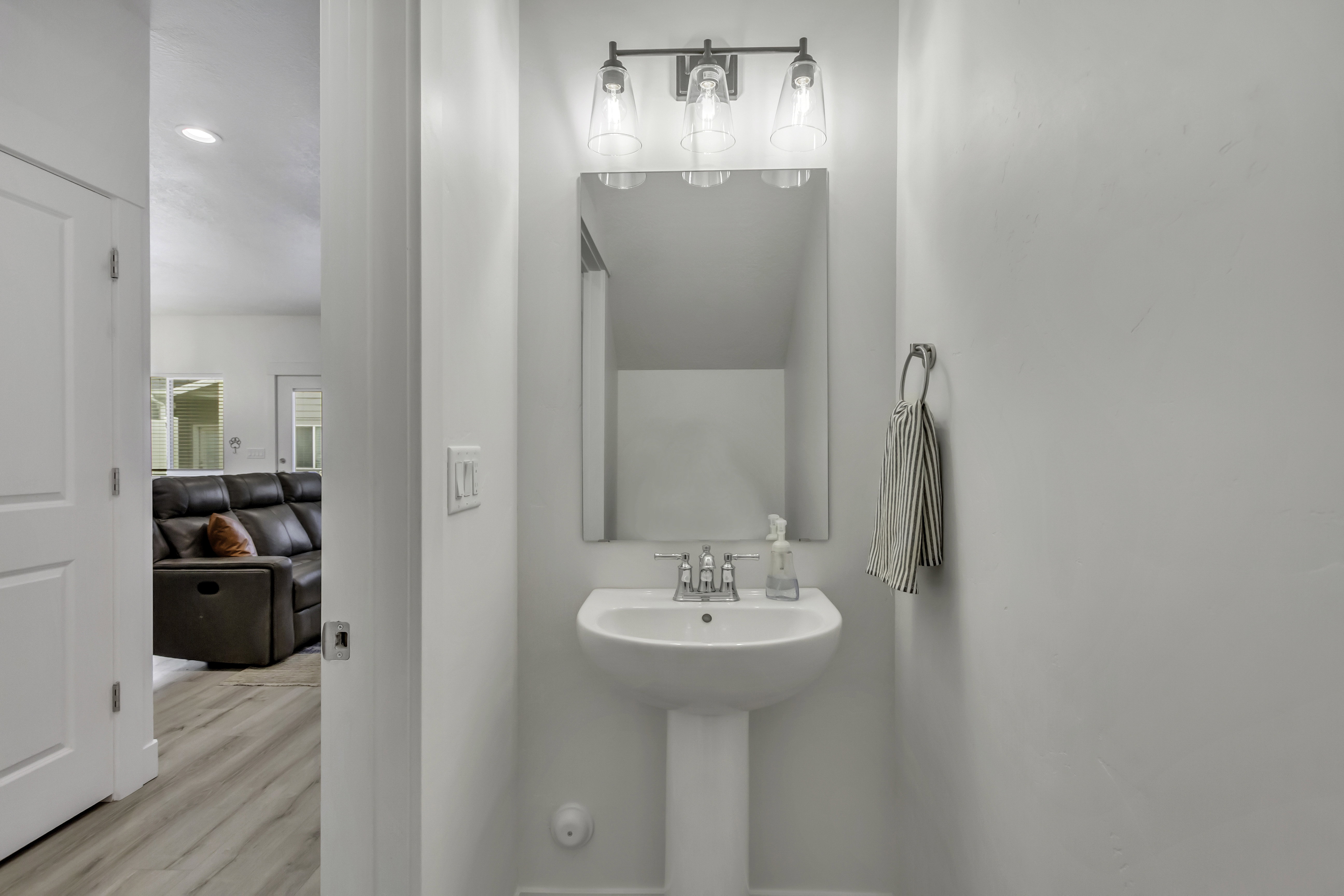 Pedestal sink with chrome faucet, complemented by an overhead three-bulb vanity light fixture