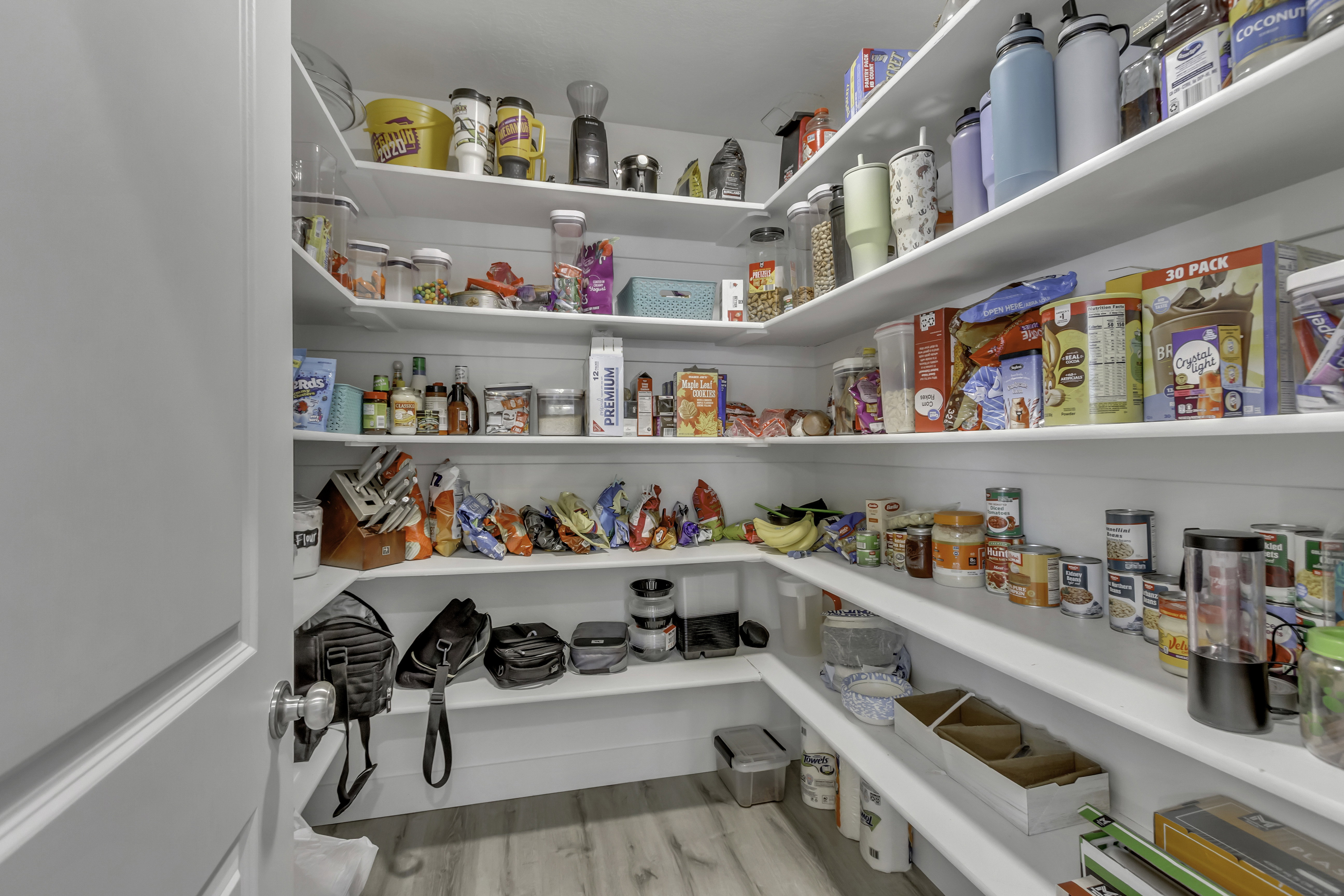 Spacious walk-in pantry featuring white shelving, light wood-finish flooring, and white walls