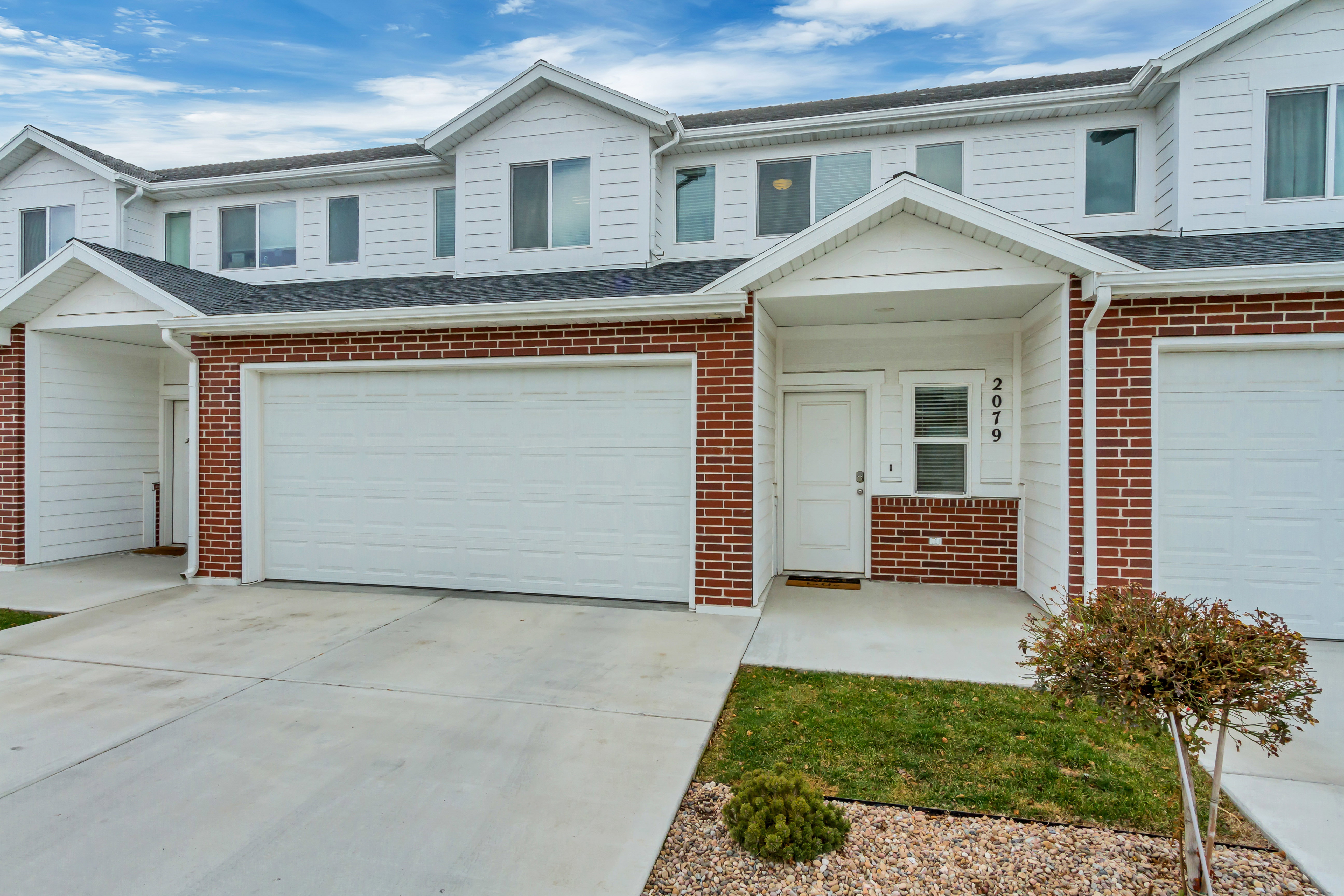 Multi-level townhouse exterior featuring a brick and siding facade, a covered entry, an attached garage, and a concrete driveway