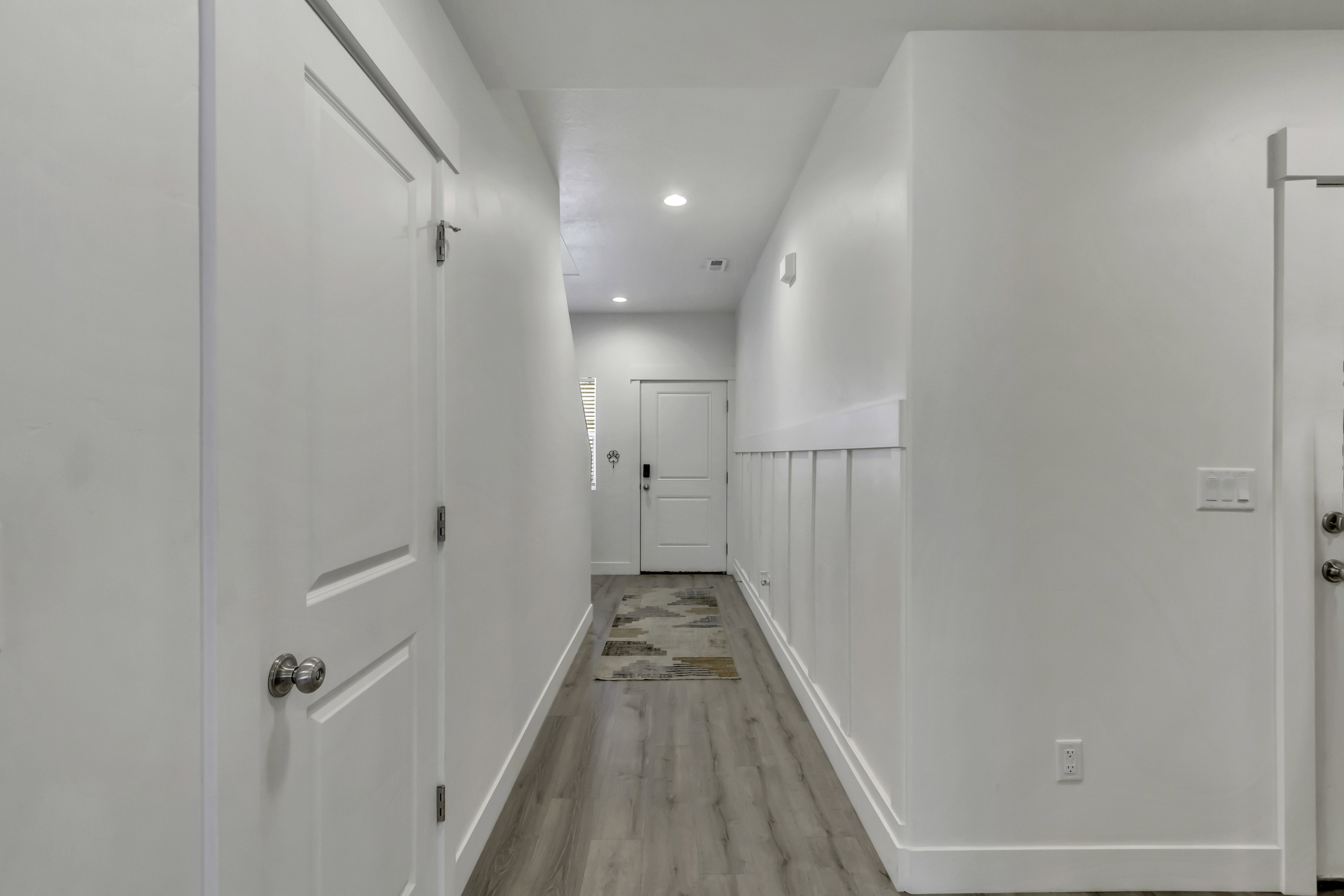 Hallway featuring wood-finish flooring, white panel-style doors, recessed lighting, and wainscoting detail