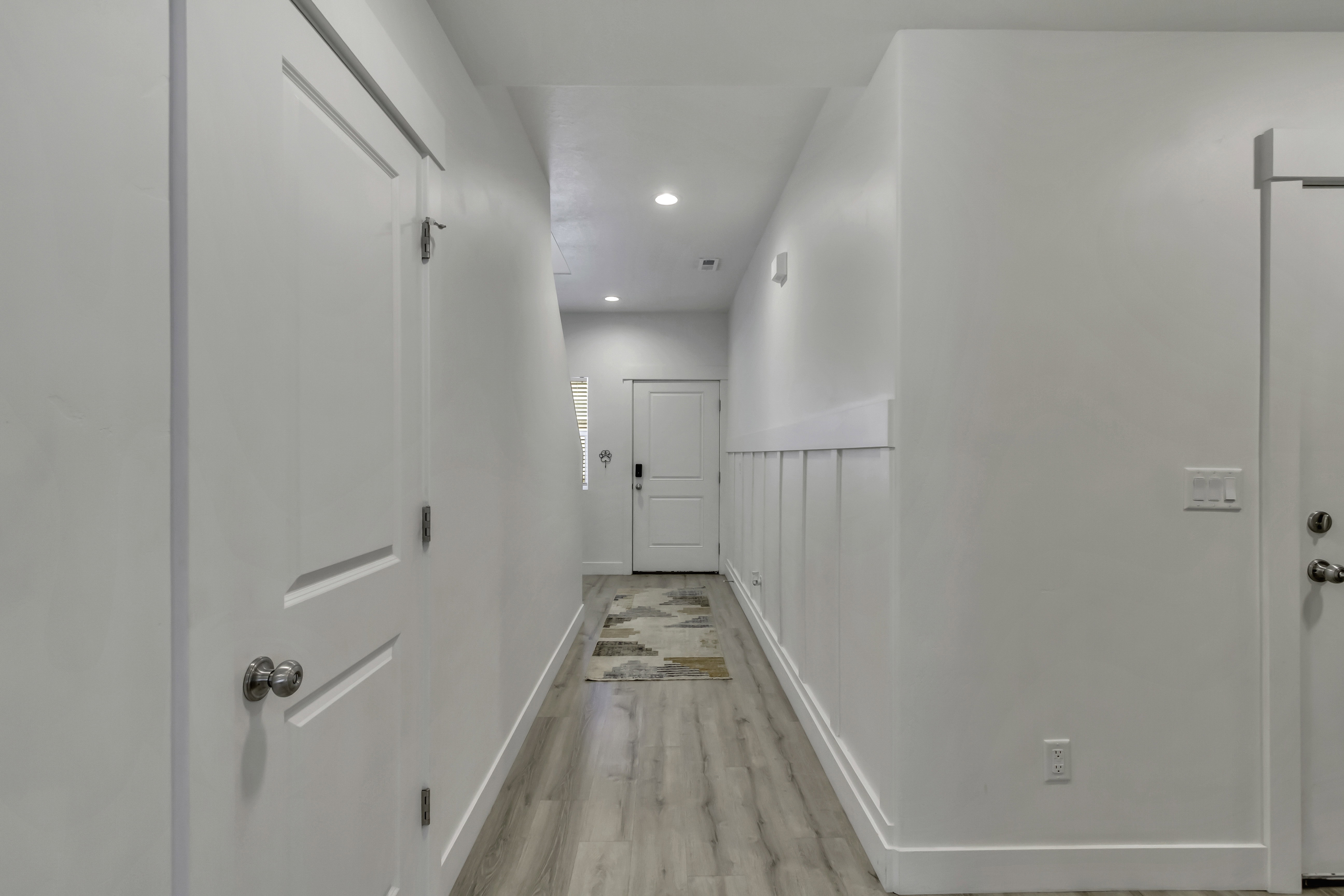 Hallway featuring light wood-finish flooring, recessed lighting, white walls, and wainscoting detail
