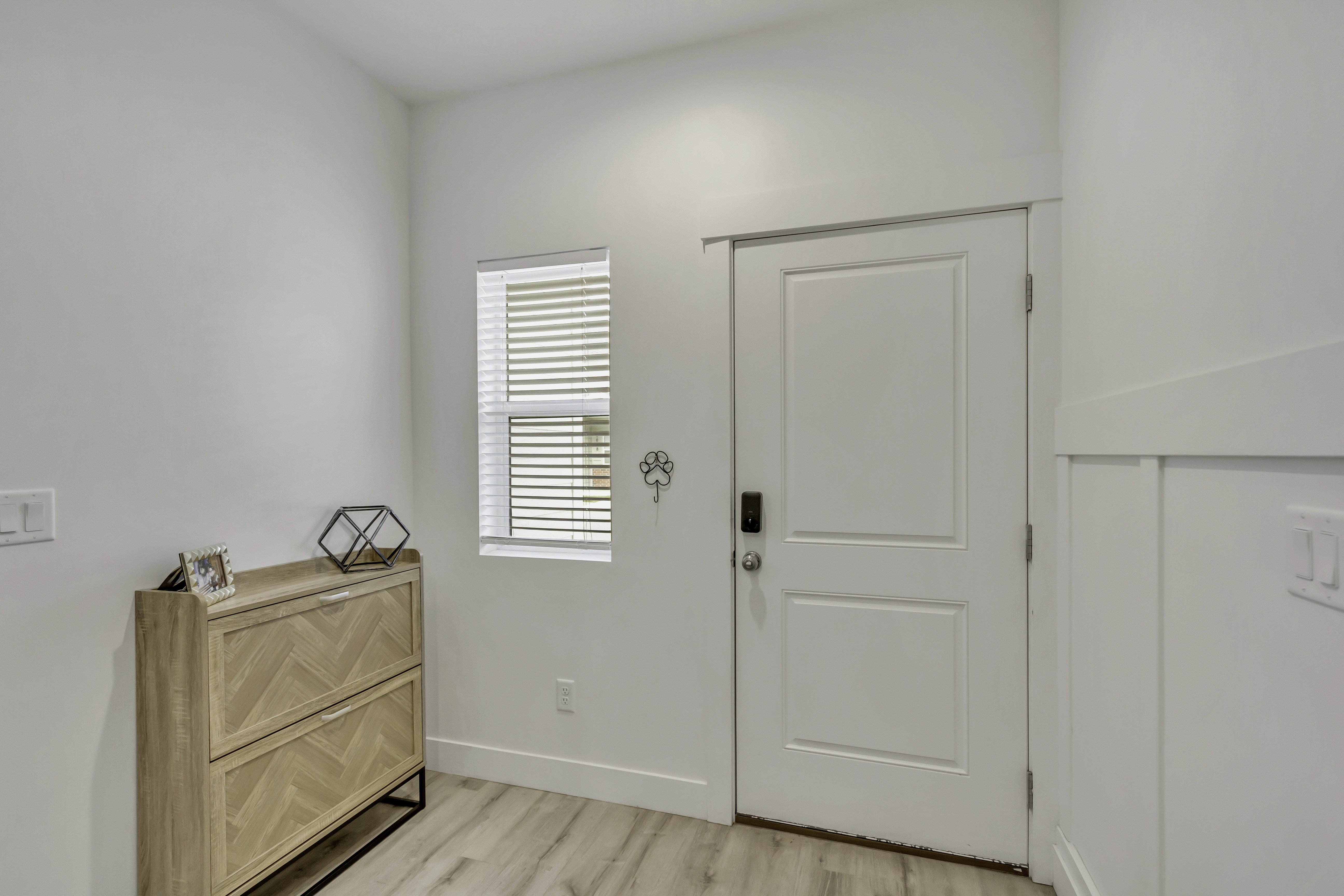 Entryway featuring a white paneled door, light wood-finish flooring, a window with blinds, and white board and batten wall detailing
