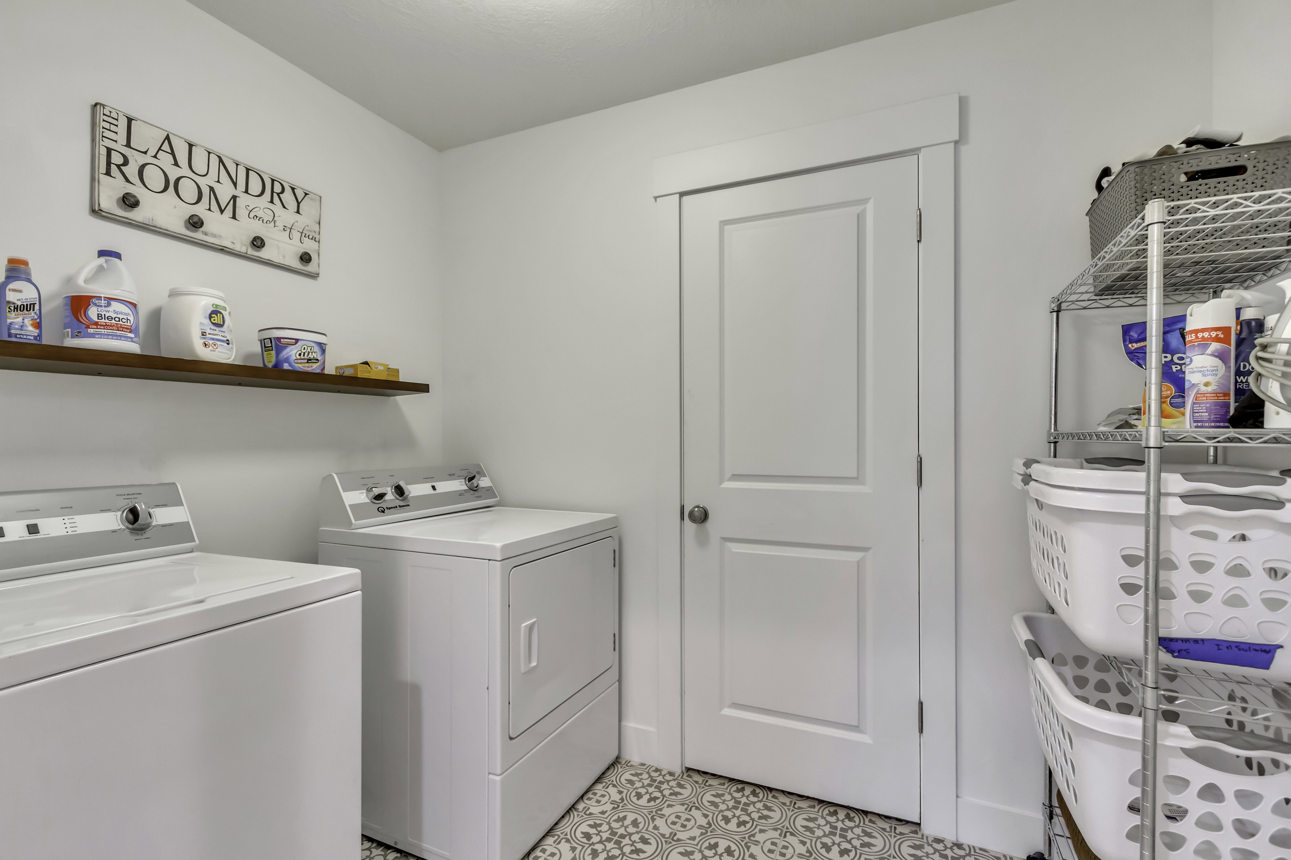 Functional laundry space featuring decorative floor tiling, a floating wood-finish shelf, and a painted door with a contemporary trim