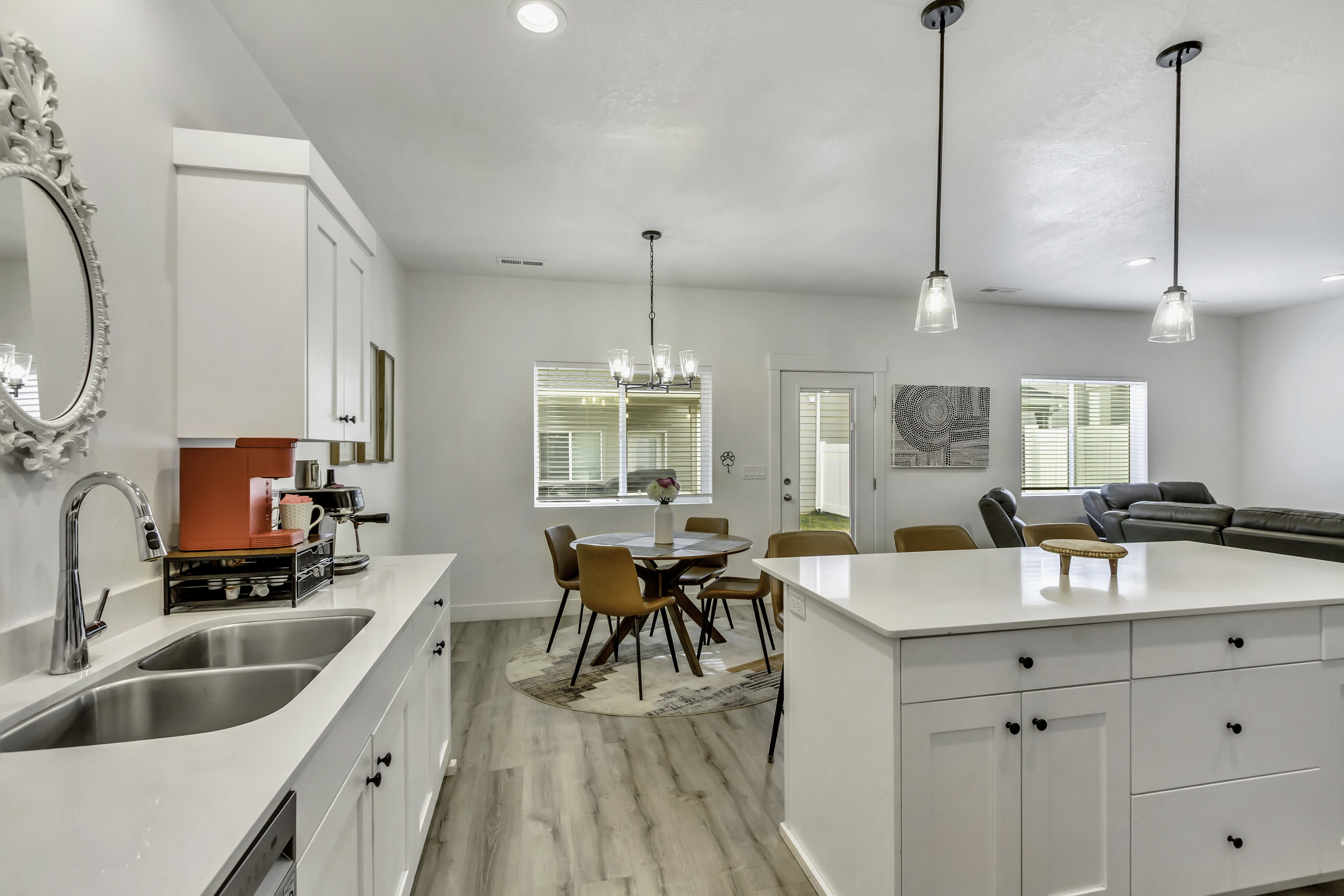 Open-concept kitchen featuring white cabinetry, light-toned wood-finish flooring, a double basin stainless steel sink, and a central island with an integrated countertop