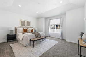 Spacious bedroom featuring light-toned carpet flooring, a large window with white blinds, recessed lighting, and a tray ceiling