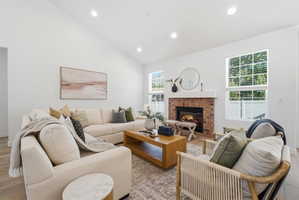 Vaulted ceiling living area featuring a brick fireplace with a white mantel, recessed lighting, wood-finish flooring, and multiple windows