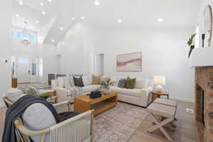 Great room featuring vaulted ceilings, recessed lighting, light wood-finish flooring, a brick fireplace with a white mantel, and a two-story entryway with a decorative chandelier