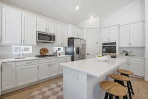 White shaker cabinetry with brushed nickel hardware, stainless steel appliances, light-toned wood-finish flooring, and a central island with a solid surface countertop