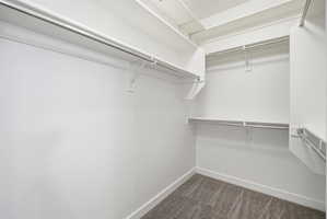 Walk-in closet featuring multiple clothing rods, integrated shelving, white walls, white baseboards, and grey carpet flooring