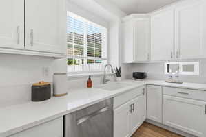 Contemporary kitchen featuring white shaker cabinetry with brushed nickel hardware, light-toned countertops, an undermount sink with a stainless steel faucet, and a stainless steel dishwasher