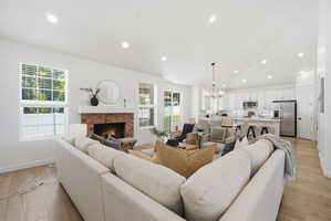 Open-concept living area featuring wood-finish flooring, a brick fireplace with a white mantel, and recessed lighting