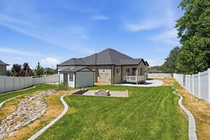 Expansive backyard with a manicured lawn, white vinyl fencing, a concrete patio, and a stone fire pit