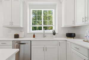 Bright kitchen featuring white cabinetry, light countertops, a stainless steel sink with a gooseneck faucet, an integrated dishwasher, and a window with blinds