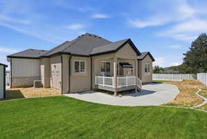 Rear exterior featuring a covered deck with white railings, a concrete patio, and a manicured lawn