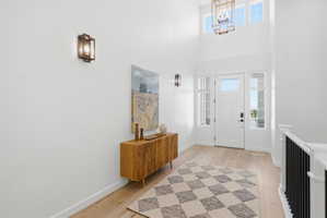 Foyer featuring high ceilings, wood-finish flooring, a white paneled entry door with sidelight windows, and a black metal spindle staircase railing