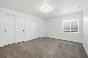 Bedroom featuring neutral tone carpeting, two sets of white sliding closet doors with black hardware, a window with blinds, and a flush mount ceiling light