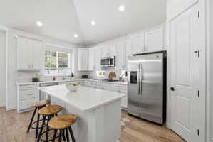 Modern kitchen featuring a central island, white cabinetry, stainless steel appliances, recessed lighting, and wood-finish flooring