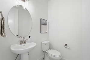 Pedestal sink with brushed nickel faucet, large round mirror, and overhead vanity lighting