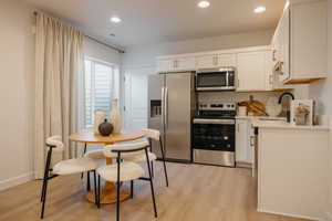 Contemporary kitchen featuring white cabinetry, stainless steel appliances, light-toned wood-finish flooring, recessed lighting, and white countertops