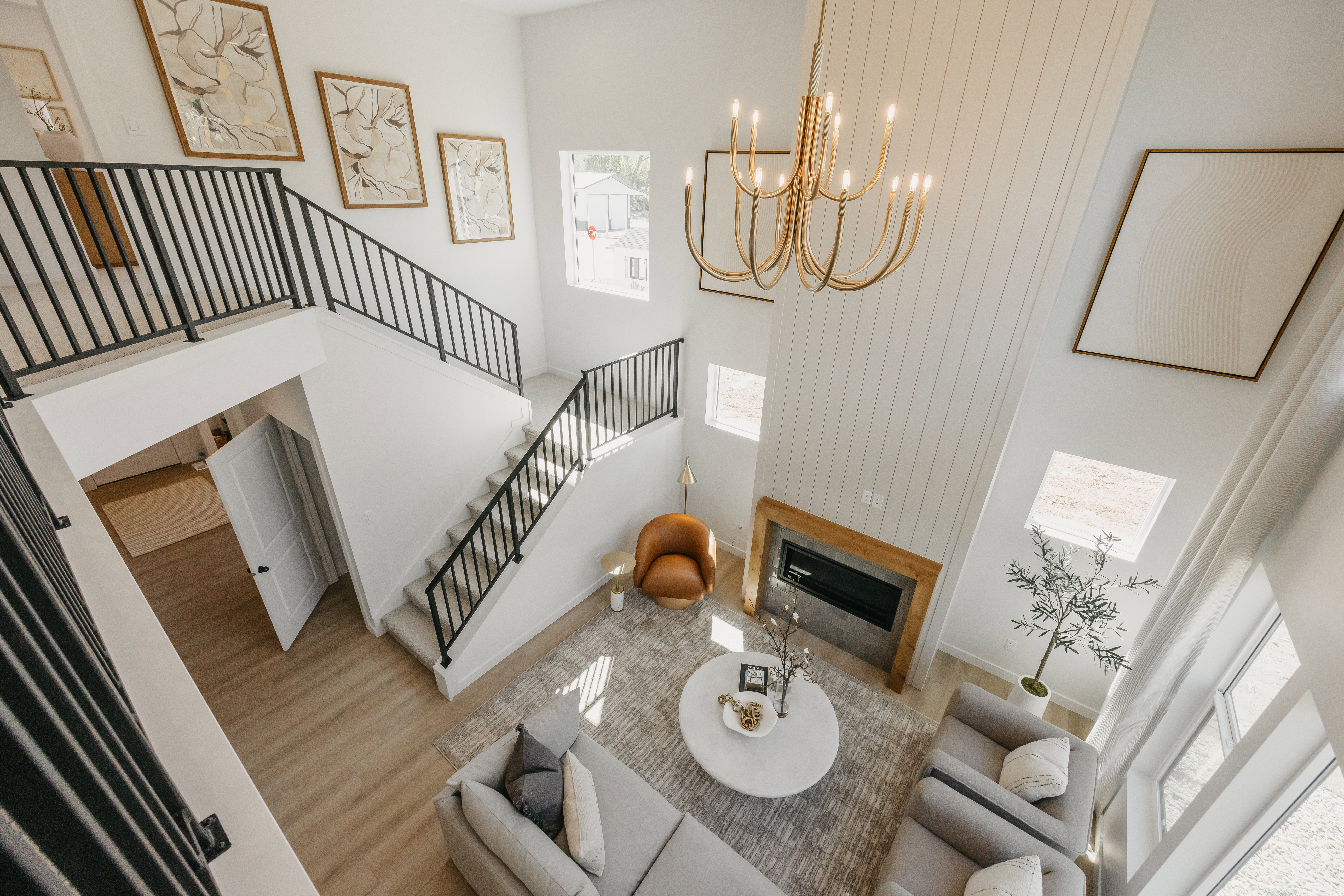 Two-story living area featuring a large brass chandelier, a fireplace with a wood mantel, wood-finish flooring, and a multi-level staircase with black railings