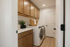 Dedicated laundry area featuring light wood-finish cabinetry with gold-tone hardware, white countertops, recessed lighting, and light wood-finish flooring