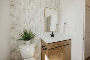 Powder room featuring a single vanity with a white countertop, an undermount sink, a matte black faucet, and a gold-framed mirror