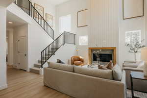 Two-story living area featuring a fireplace with a wood surround and tile hearth, a high ceiling with vertical paneling, and an open-tread staircase with black iron railings