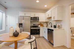 Modern kitchen featuring stainless steel appliances, white cabinetry with gold-tone hardware, and a black faucet