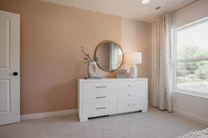 Spacious room featuring neutral wall tones, plush carpeting, a large window, recessed lighting, and a solid core door with black hardware