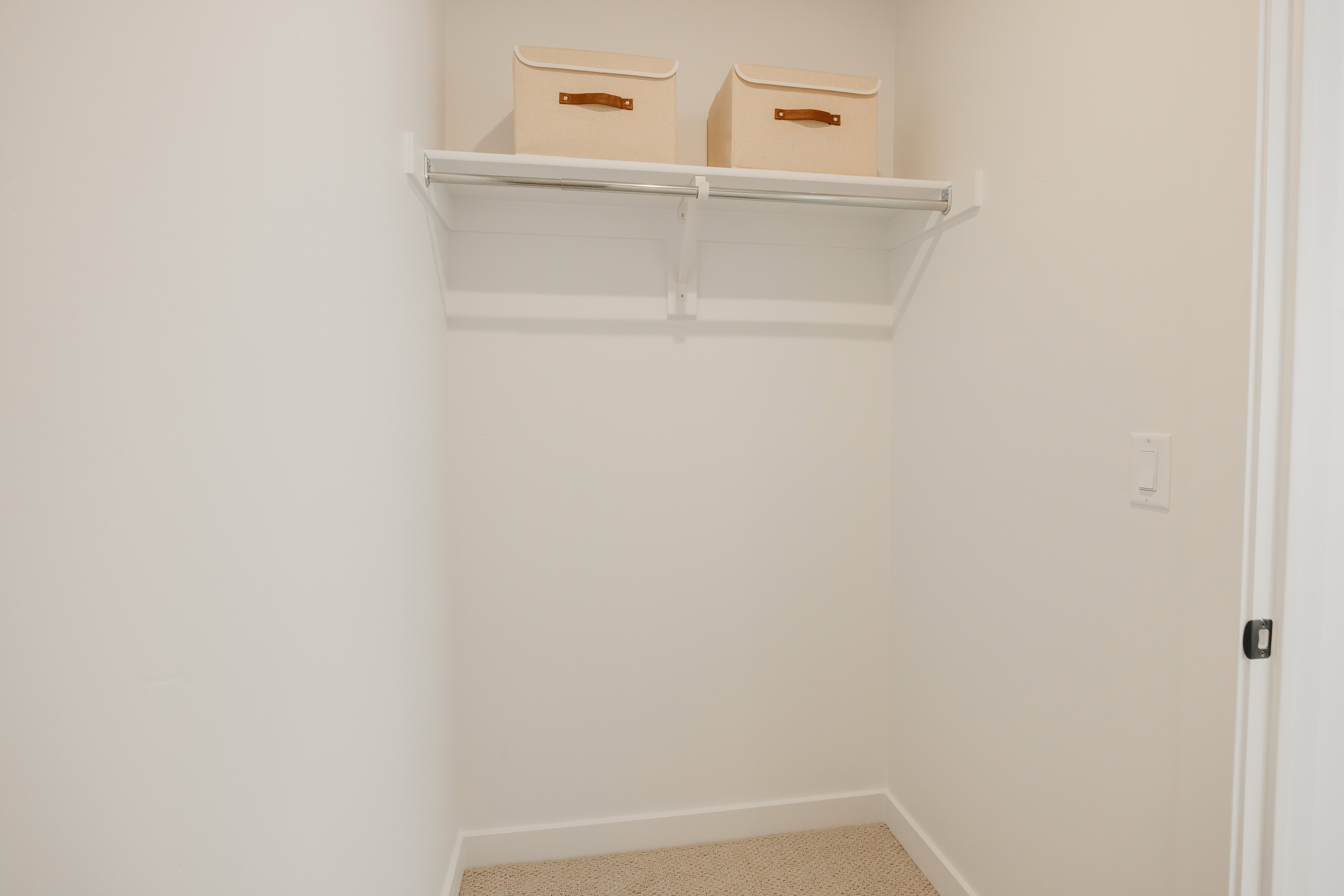 Walk-in closet featuring a white shelf and hanging rod, light-colored carpeting, and white baseboards