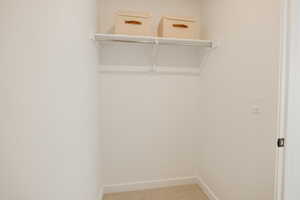 Walk-in closet featuring a white shelf and hanging rod, light-colored carpeting, and white baseboards