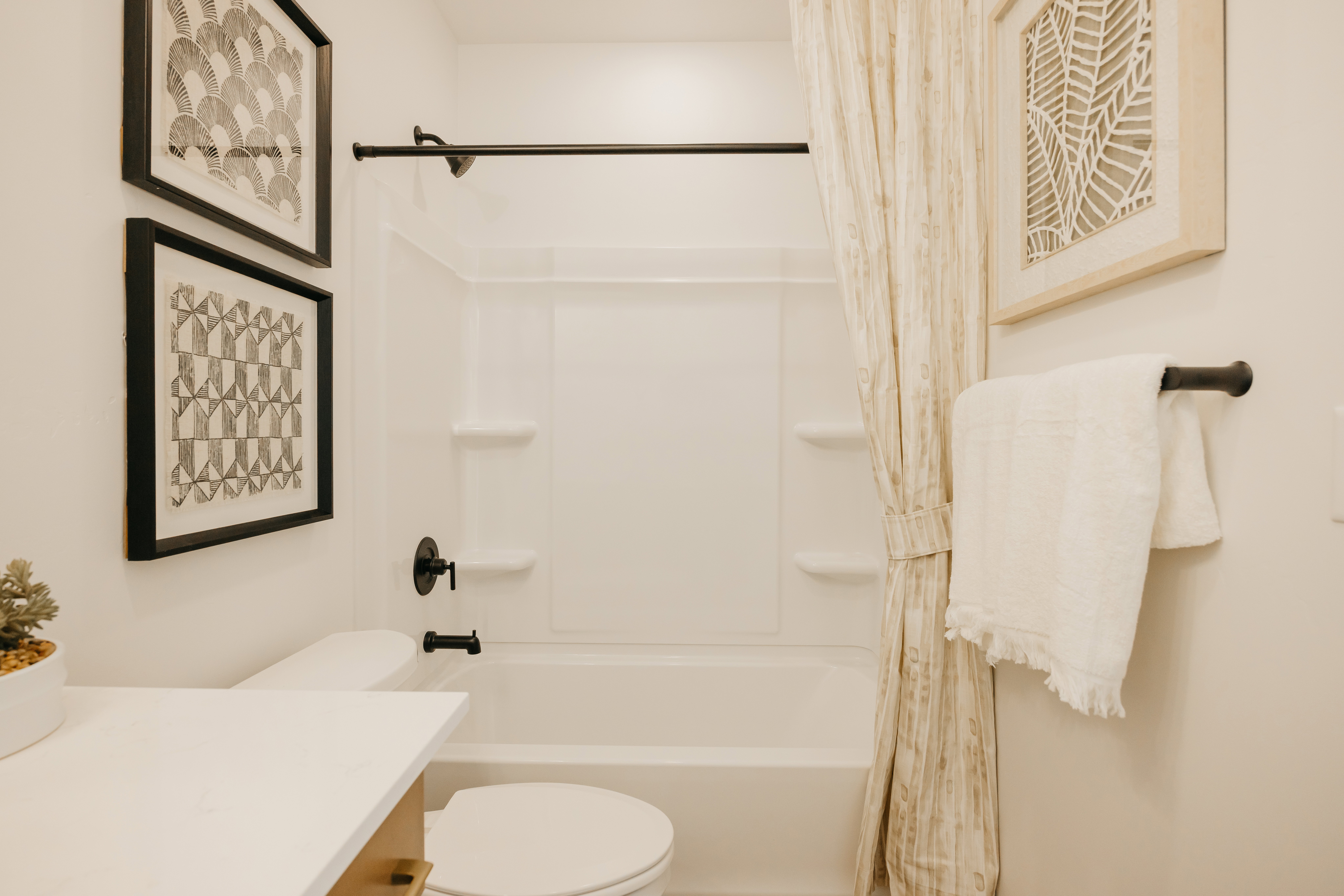 Bathroom featuring a white tub/shower combination with integrated shelving, matte black fixtures, and a white toilet